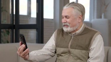 Mutlu, yakışıklı, yaşlı, gri sakallı, emekli olmuş bir adam cep telefonuyla video görüşmesi yapıyor, akrabalarıyla iletişim kuruyor ve uzun süreli bakım tesislerinde dinlenirken paylaşıyor.