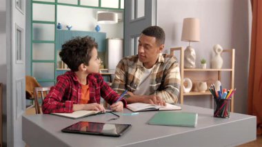 Yakışıklı Afrikalı Amerikalı babaya özel ders ödevi vermek, akıllı okul çağındaki siyahi oğlanın ödevlerini yapmasına yardım etmek aile içinde birlikte eğitim görürken.