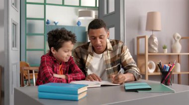 Yakışıklı Afrikalı Amerikalı baba ve şirin okul çağında siyahi oğul birlikte çalışıyor, matematiksel örnekleri çözüyor ve ödevlerini evde yaparken egzersiz kitabına çözümler yazıyor..