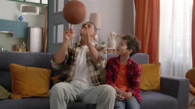 Yetenekli, neşeli siyahi baba neşeli Afrikalı Amerikalı oğluna numara yapıyor, basketbol topunu parmaklarıyla çeviriyor birleşik aile ise evde eğleniyor ve eğleniyor..