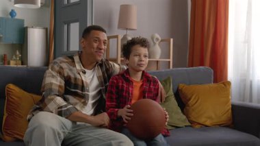 Yakışıklı Afro-Amerikan baba ve neşeli, genç, siyah oğlu kanepede oturmuş, evcil odada basketbol maçı seyrediyor..