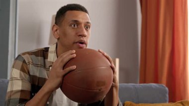 Afro-Amerikan erkek basketbol fanatiğinin portresi televizyonda basketbol maçı izliyor, favori takımı destekliyor ve zaferi jest yaparak kutluyor, evdeki heyecan ve neşeyi ifade ediyor..