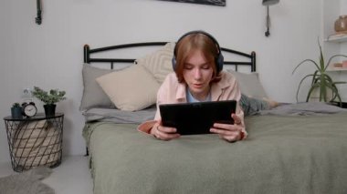 Kablosuz kulaklık takan, tablet bilgisayarda oyun oynayan ve evdeki takım arkadaşlarıyla iletişim kuran hoş bir genç kız..