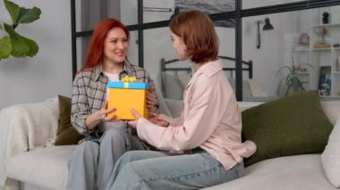 Neşeli kızıl saçlı olgun anne hediyesini alıyor, doğum günü hediyesi için teşekkür ediyor ve sevimli genç kızı kucaklıyor, evde mutluluk ve heyecanı ifade ediyor..