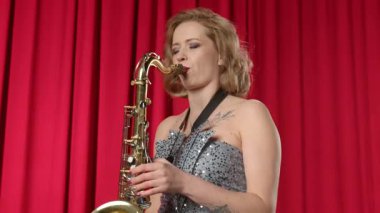 Tutkulu yetenekli kadın saksafoncu modaya uygun kıyafetler giyiyor, alto saksafon çalıyor ve konser salonundaki spot ışıklarıyla aydınlatılmış sahnede caz müziği çalıyor.