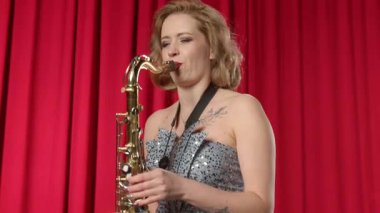 Çekici sarışın müzisyen portresi duygusal olarak saksafon çalan, canlı müzik çalan, sahnede performansı bitiren ve neşeli bir gülümsemeyle bakan .