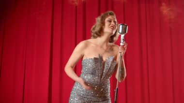 Şen sarışın, zarif, uzun elbiseli, klasik mikrofonlu bir şarkıcı. Sahnede canlı performans sergilerken duygusal olarak şarkı söylüyor. Duman bulutları arasında..