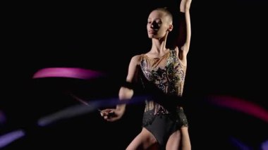 Zarif ritmik jimnastikçinin portresi zarif taytlarıyla desenli kurdele ile siyah arka planda yılan figürleri yapıyor..