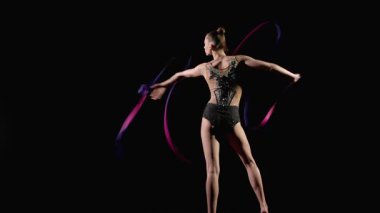 Siyah arka planda ritmik jimnastik yılanları icra eden parlak kurdeleli şık taytlı yetenekli genç bayan sporcu..