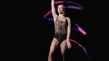 Şık giysili, kurdeleli, ritmik jimnastik elementleriyle, siyah arka planda geriye doğru yılanlar yapan yetenekli genç ritmik jimnastikçi..