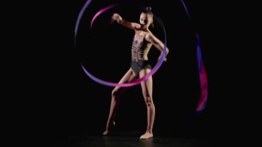 Şık giyimli zarif ritmik jimnastikçi. Şablonlu kurdeleli. Ritmik jimnastik elementler sergiliyor.