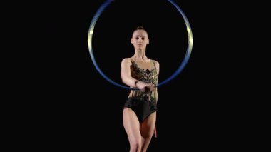 Profesyonel zarif ritmik jimnastikçinin zarif taytlı portresi, ritmik jimnastik elementler uyguluyor, siyah arka planda el etrafında parlak çemberler çiziyor..