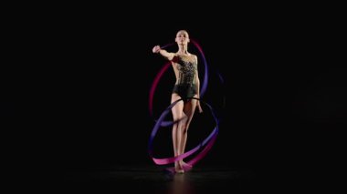 Zarif taytlı profesyonel çekici jimnastikçinin tam uzunluğunda ritmik jimnastik elementler, desenli kurdele, spiral ve yılanları siyah arka planda sergilemesi..