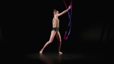 Parlak kurdeleli, çeşitli ritmik jimnastik elementleri uygulayan zarif, profesyonel jimnastikçinin tam uzunluğu, siyah arka planda yılanlar ve spiraller..