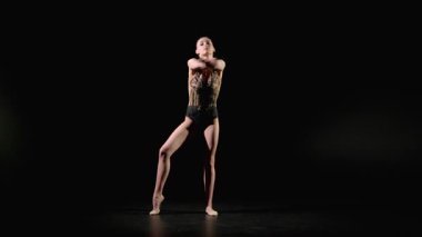 Zarif giyimli zarif bayan sporcu zarif bir şekilde klüplerle ritmik jimnastik elementleri sergiliyor, siyah arka planda okçu pozisyonunda geriniyor..