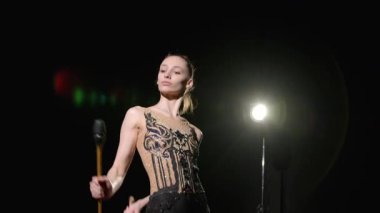 Kendine güvenen şık taytlı güzel bayan sporcu. Küçük atlama ve yakalama teknikleriyle ritmik jimnastik yapıyor. Siyah arka planda spot ışıklarıyla aydınlatılıyor..
