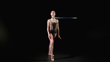 Profesyonel çekici jimnastikçi zarif taytlı, ritmik jimnastik yapan, boynun etrafında dönen parlak çemberli, siyah arka planda tek elle dönen.