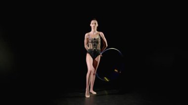 Şık taytlı, zarif, güzel jimnastikçi ritmik jimnastik elementleri sergiliyor, iki eliyle dönen ve hokkabazlık yapan, siyah arka planda arkaya geçen..