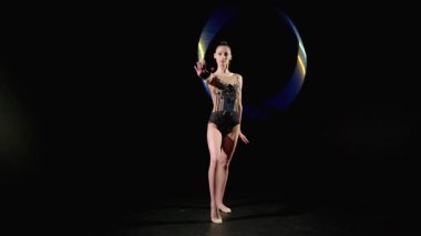 Tam boy profesyonel büyüleyici ritmik jimnastikçi şık bir tayt, ritmik jimnastik elementler, siyah arka planda elleri etrafında dönen parlak halka.