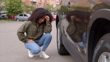 Sinirli, çekici, Afro-Amerikan kadın şoför. Park halindeki aracın yanında oturuyor. Trafik kazasından sonra araba sürerken oluşan çizikleri ve ezikleri kontrol ediyor..