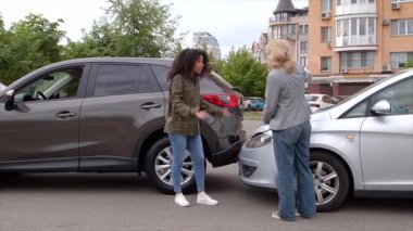 Sinirli Afrikalı Amerikalı kadın sürücü ve sinirli orta yaşlı kadın şehir caddesinde araba kazası sonrası duygusal olarak tartışıyorlar, araba kazası için birbirlerini suçluyorlar.