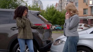 Hüsrana uğramış Afro-Amerikan kadın ve orta yaşlı kadın sürücü yol yardımı için arıyor, yolda araba kazası sonrası sigorta hattıyla akıllı telefonlardan konuşuyor..