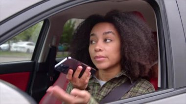 Sürücü koltuğunda oturan, trafik sıkışıklığında araba sürerken cep telefonundan sesli mesaj kaydeden kendinden emin Afrikalı Amerikalı kadın girişimci..