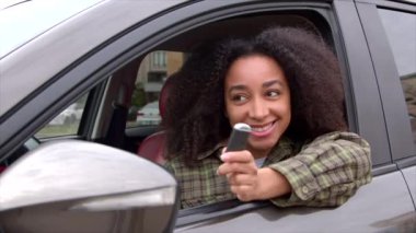 Heyecanlı çekici Afrikalı Amerikalı kadın sürücü yeni bir araçta oturuyor, elinde anahtarsız giriş sabitleyicisi, araba galerisinde araba aldıktan sonra mutluluk ve neşe ifade ediyor..