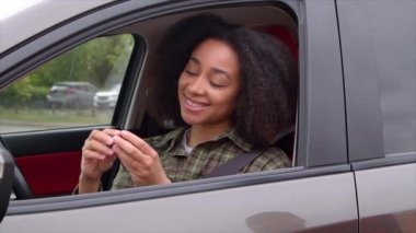 Afro saç stili neşeli, çekici Afro-Amerikan kadın sürücü koltuğunda oturuyor, satın aldıktan sonra araba satıcısından anahtar alıyor, heyecan ve mutluluğu ifade ediyor..