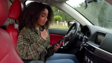 Başarılı bir Afrikalı Amerikalı kadın girişimci arabada oturuyor, dijital tablet ve finansal verileri kullanarak çevrim içi ağ kuruyor, yolculuk sırasında iş kararları üzerinde kafa yoruyor.