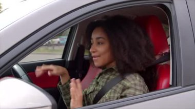 Afro saç stili olan güzel Afrikalı Amerikalı kadın sürücü, arabada oturuyor, müzik dinlemekten hoşlanıyor, şarkı söylüyor ve şehirde araba sürerken sallanıyor..