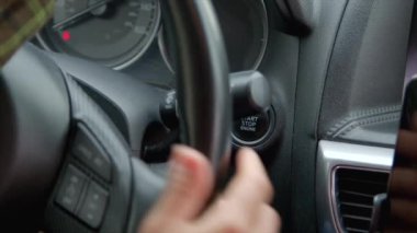 Kadın parmak, araba motoru çalıştırma düğmesine basar, direksiyonu sıkıca tutar ve yola koyulur. Arka görünüm.