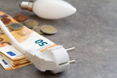 Elektrik prizi, ampul ve para, yükselen enerji fiyatları kavramı