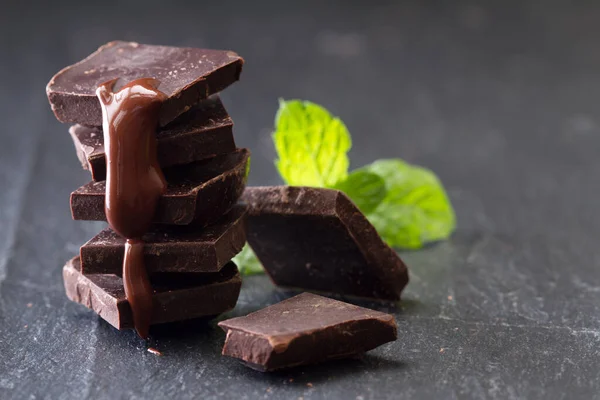 黒を背景にミントの葉とチョコレートソースとダークチョコレートのいくつかのキューブ — ストック写真