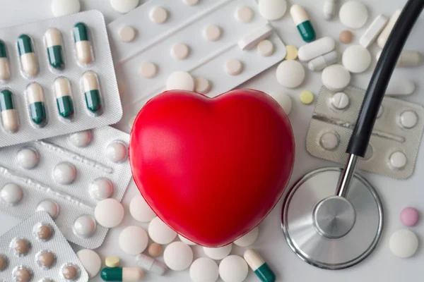 Red heart and  stethoscope on background of various pills