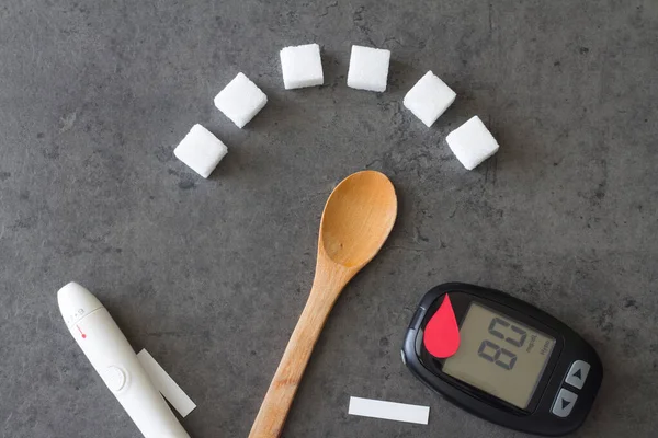 Sugar cubes with spoon indicating high sugar level, red blood drop and glucometer, diabetes concept