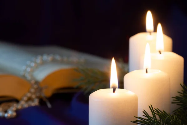 Four burning Advent candles with open Bible and rosary in background, religious symbol concept