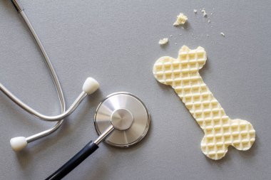 Bone-shaped waffle and stethoscope, fragile, brittle bones, osteoporosis, creative concept clipart