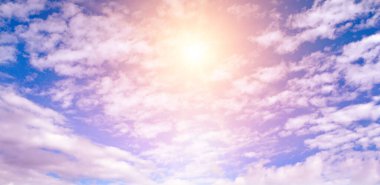 Mavi gökyüzünde beyaz kümülüs bulutları ve parlak bir güneş var. Geniş resim.