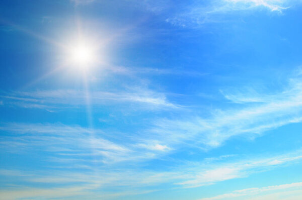There are white cumulus clouds and a bright sun in the blue sky.