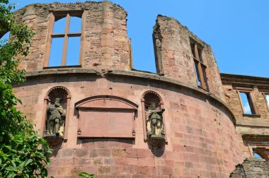 An ancient, partially ruined brick structure from Heidelberg Castle in Germany, with large arched windows framed by weathered stone, set against a bright blue sky. clipart