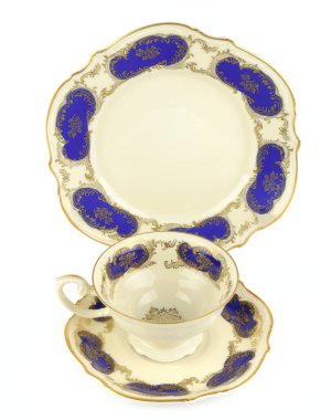 Altın saplı ve kenarlı beyaz porselen bir çay fincanının minimalist natüralisti, uyumlu bir çay tabağının üzerinde dinleniyor. Görüntü temiz ve zarif.