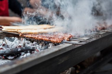 Delicious Adana kebabs are grilling on a barbecue with smoke, close up