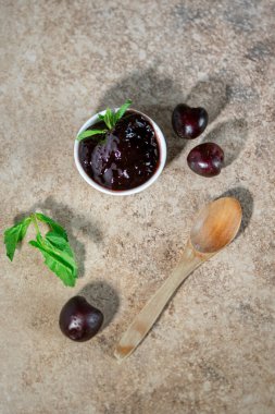 Tahta arka planda tahta kaşıkla beyaz bir kasede vişne reçeli, yakın çekim, bakış açısı fotoğrafçılığı, natürmort.