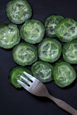 Siyah ahşap arka planda metal çatalla doğranmış taze salatalıklar, yakın çekim, görüş açısının üstünde.