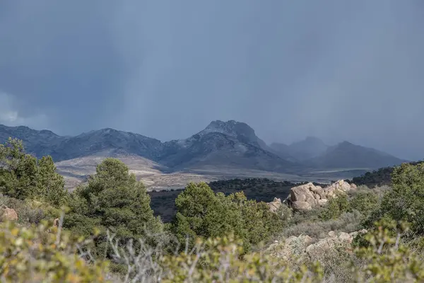 Beautiful scenic mountains with light snow and gray clouds preciptating rain while foreground is sunny in Arizona, USA