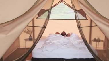 Tracking in of young Biracial woman and bearded husband sleeping in bed in glamping in morning