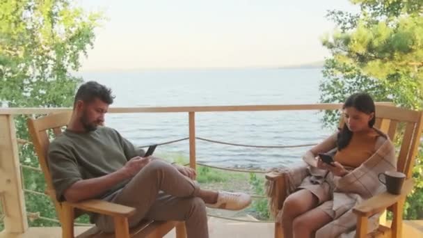 夏天阳光明媚的日子 一个中等身材的男人和他年轻的妻子坐在湖边的长椅上 他们用的是小玩意 — 图库视频影像