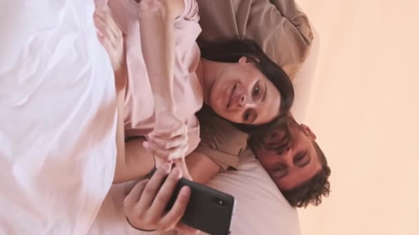 幸せな若い英雄のカップルの中には ホテルの部屋に横たわって 笑顔で 話して スマートフォンを使用して フィードをスクロール — ストック動画