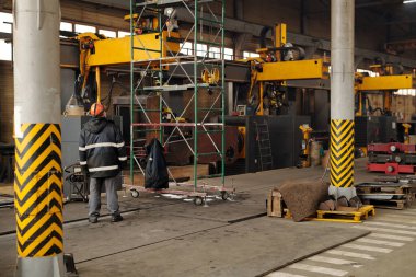 Worker of large industrial plant standing in front of technical construction and part of huge machie while working in warehouse
